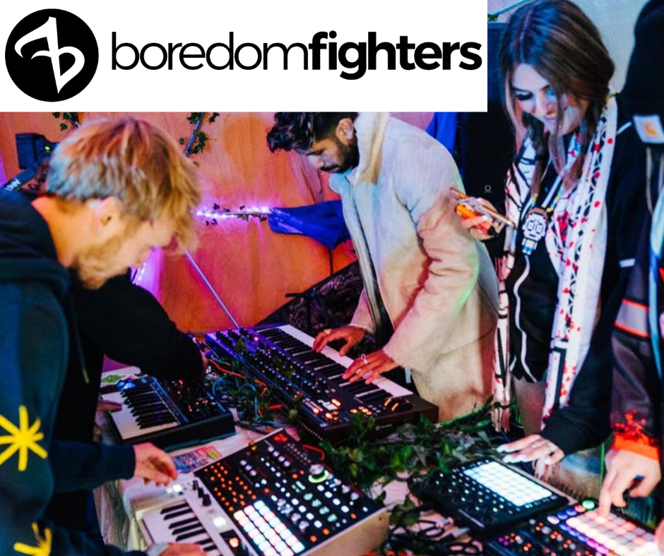 People gathered around a table with keyboards and music production panels with the boredomfighters logo across the top