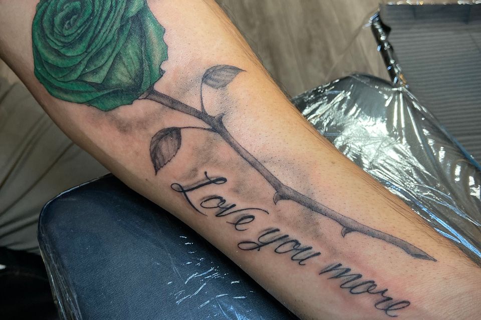 Image of a mans forearm with a green rose on a black & Grey stem with thorns and the words "I Love You More" below the stem of the rose
