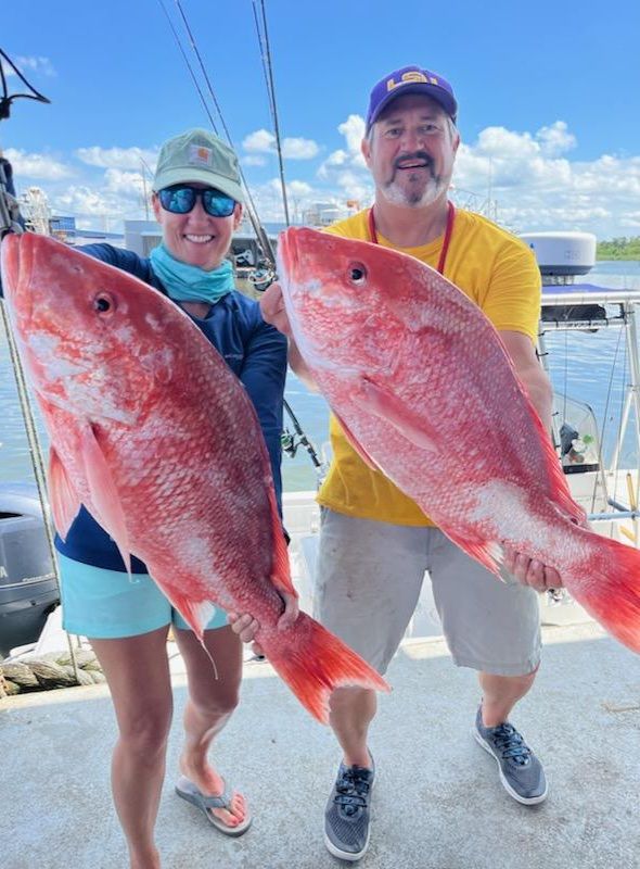 Two happy clients holding massive Red Snappers caught from the Gulf of Mexico in Louisiana.