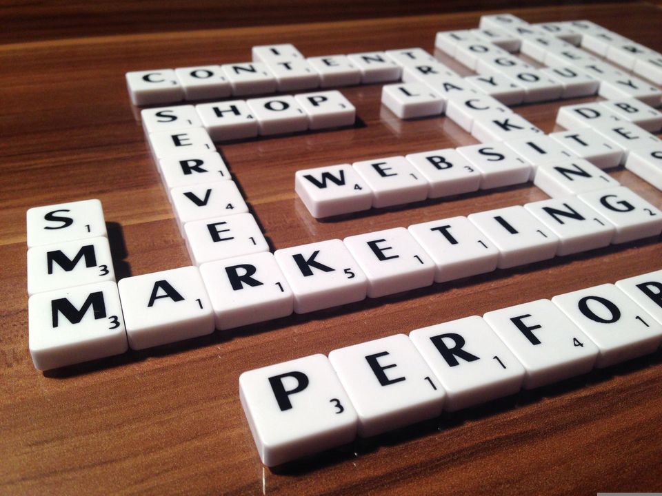 table with scrabble tiles arranged in a way so the word marketing is in the center of the table. The words server, shop, website, tracking, performance and more web presence related words can be read as well.