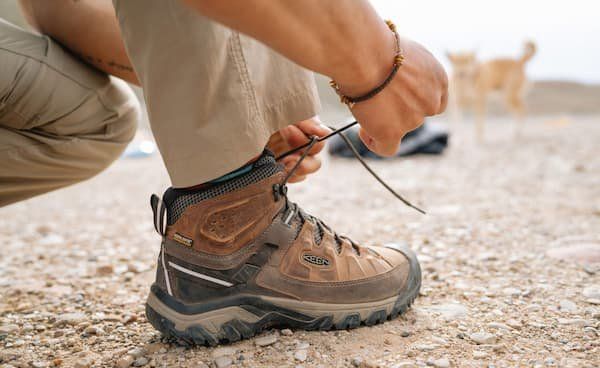 A person lacing up their KEEN hiking boot image seen from the shin down.