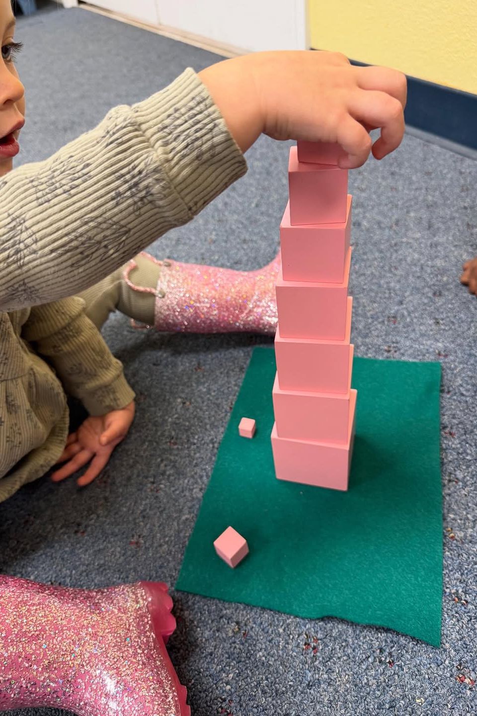 Toddler stacking the Montessori pink tower cubes during a sensorial building activity in Palmdale CA