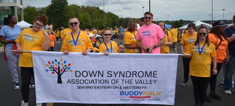 Buddy Walk participants holding a Down Syndrome Association of the Valley banner at a community awareness event.