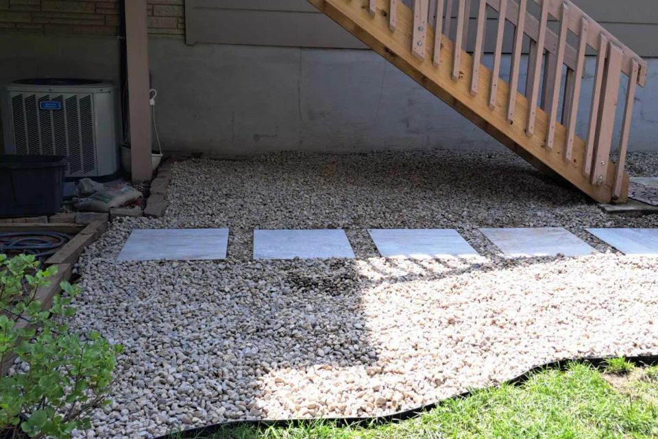 Backyard gravel area with square stone pavers installed beneath a deck for easy access.