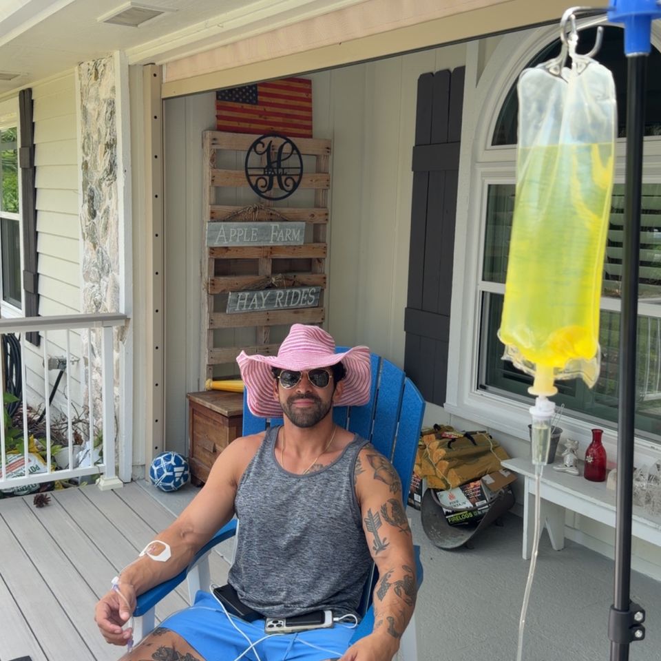 Man in a pink hat receiving a mobile IV drip on a home front porch in Palm Beach County FL