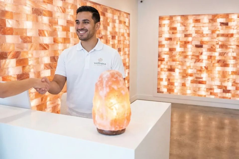 Friendly wellness center owner greeting new client at reception desk with Himalayan salt decor.
