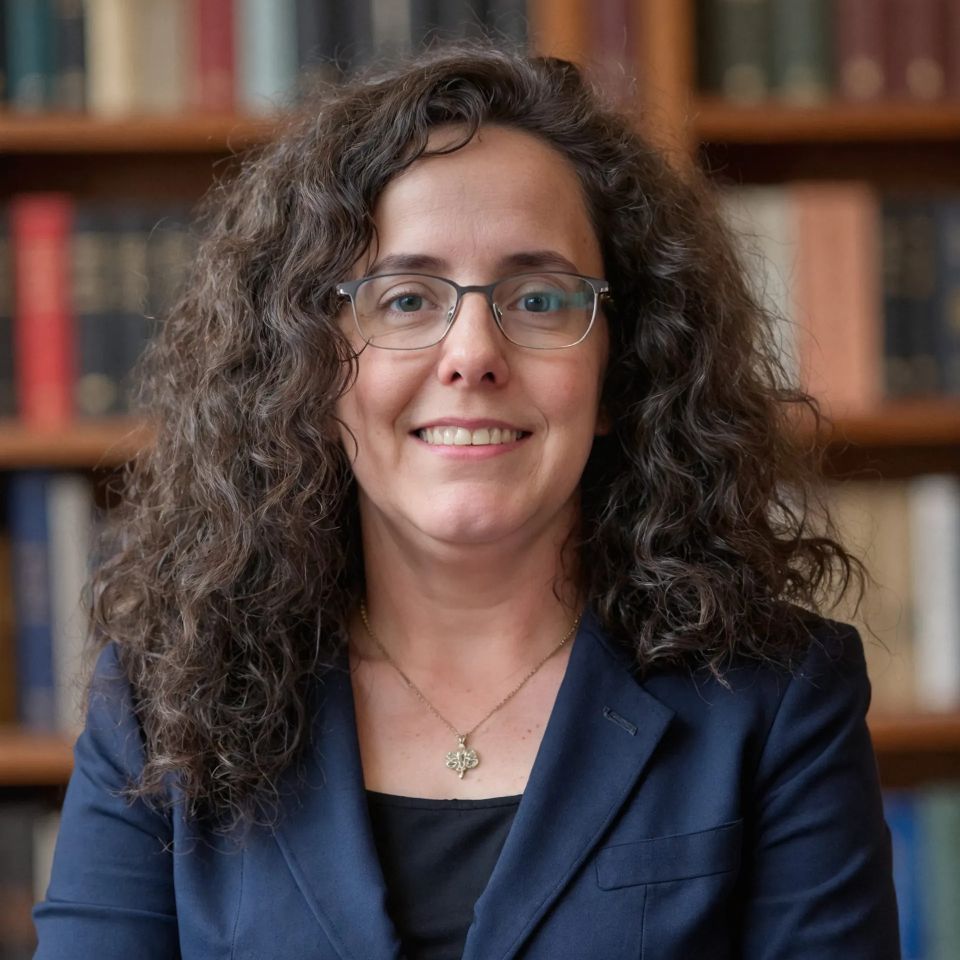  Headshot of Vicki Cochran in front a library bookshelf.  She is wearing a professional top and has glasses with wavy hair.