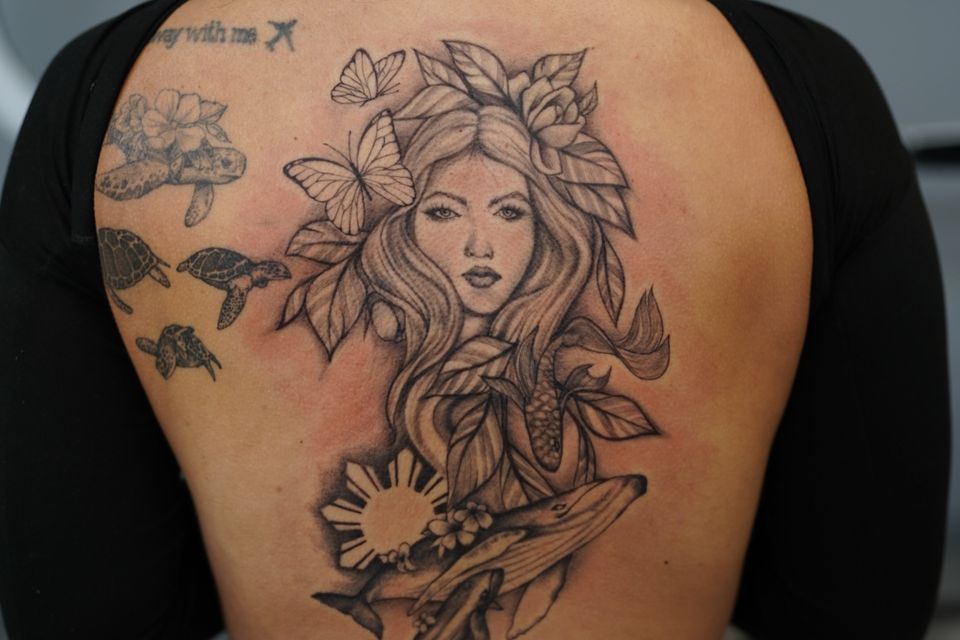 Image of a detailed black and white tattoo of a woman, butterflies, foilage, a whale and it's calf, and sea turtles