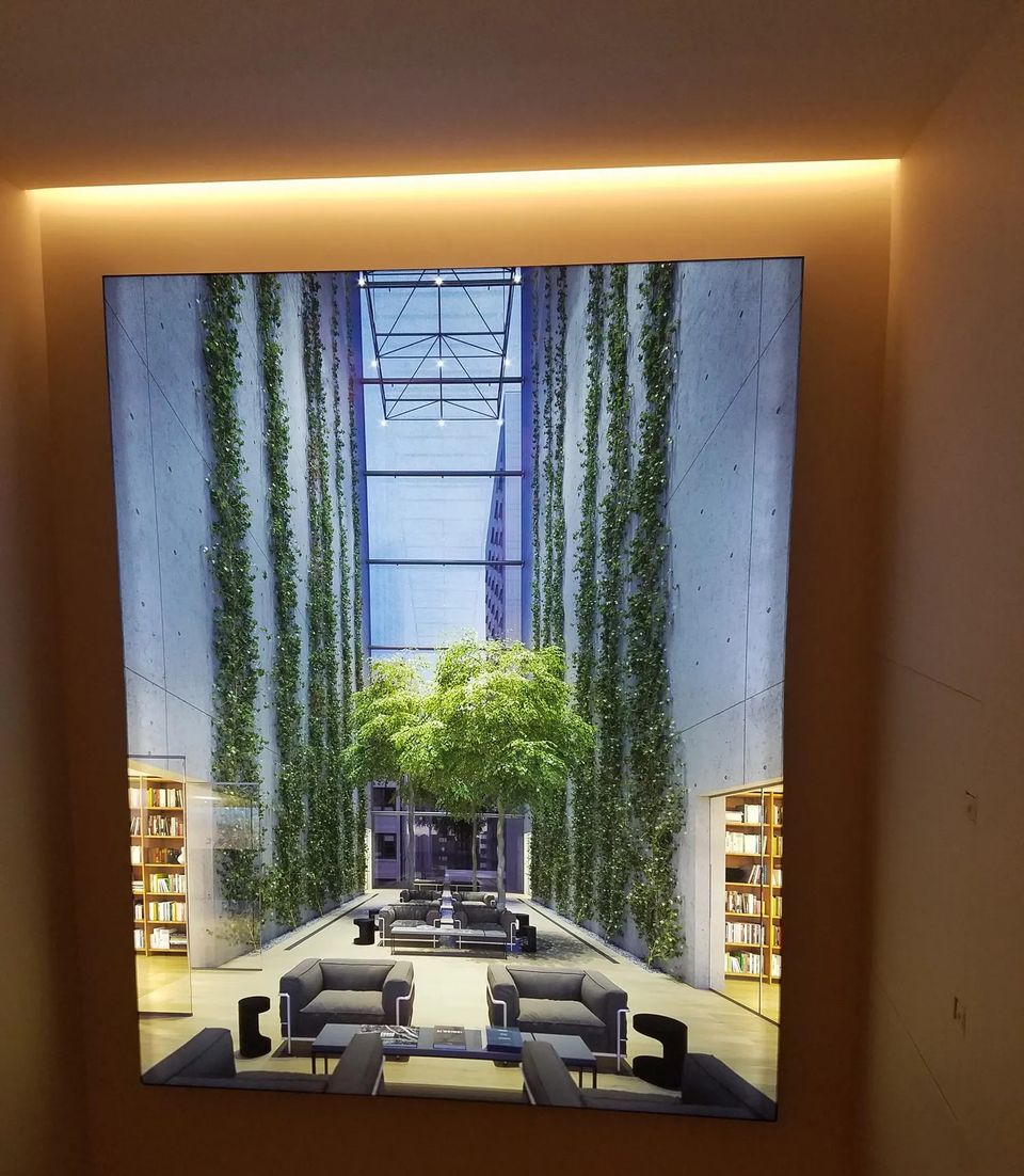 Large backlit light box showing a planted atrium, set into a recessed wall niche under a cove light in Manhattan