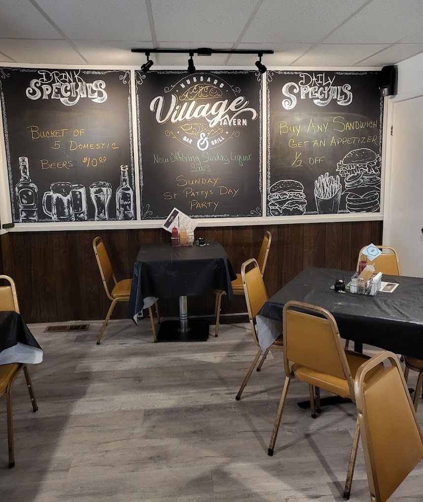 Dining area with tables and chalkboard wall showing Village Tavern drink and food specials