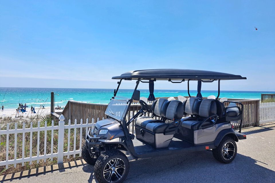 Gray six-passenger golf cart rental parked at a beach access boardwalk overlooking turquoise water in Destin Florida