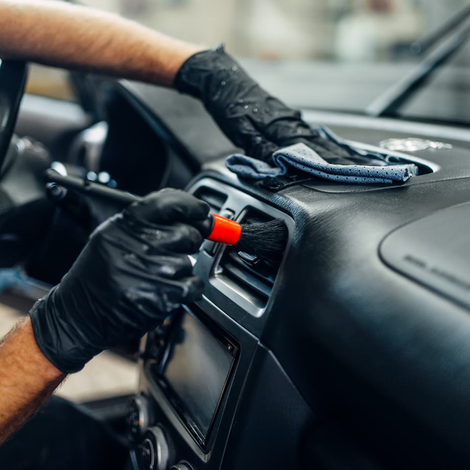 Technician cleaning a vehicle dashboard and air vents with detailing tools during interior detailing service.