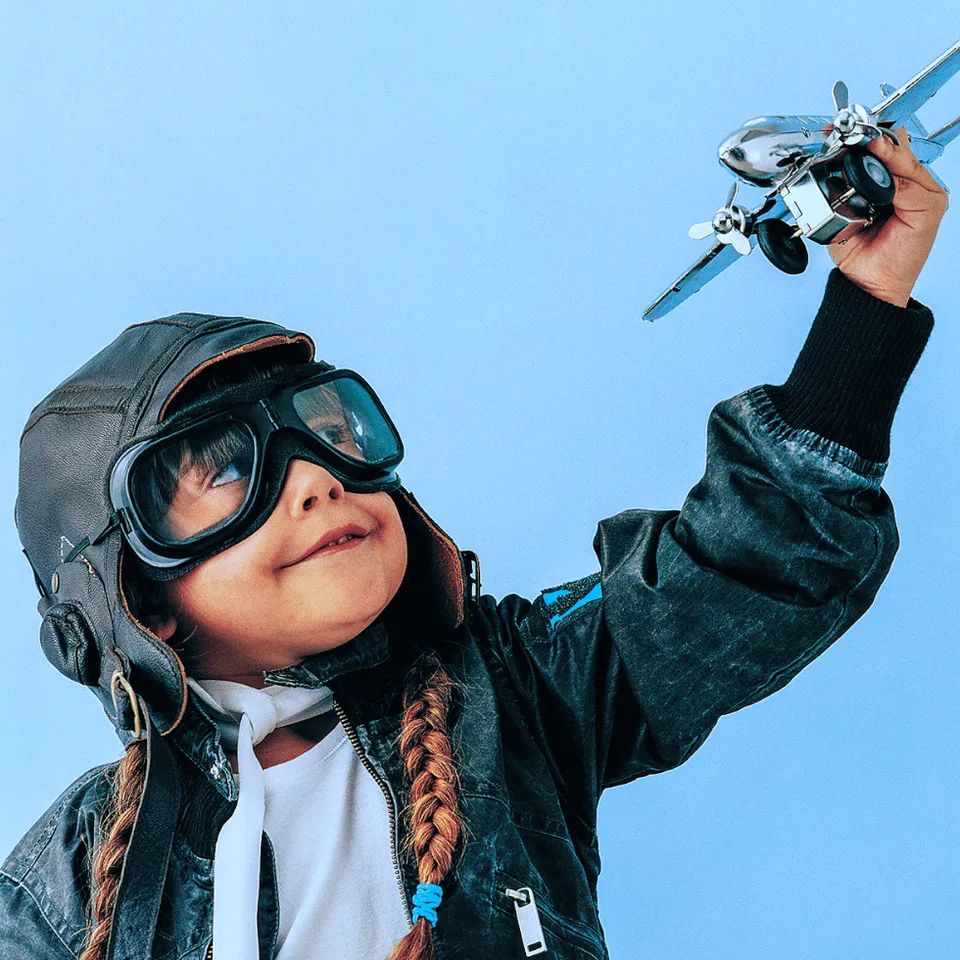Little girl wearing aviator goggles pilot hat playing with model plane