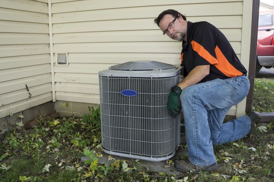 An HVAC tech outside working on the AC system at someone's house