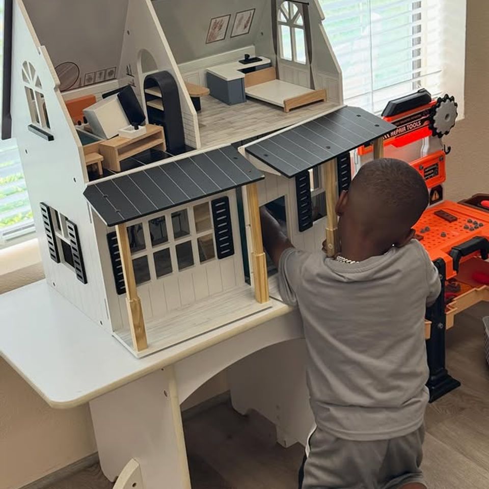 Young boy playing with a large wooden dollhouse during preschool free choice time in Palmdale CA
