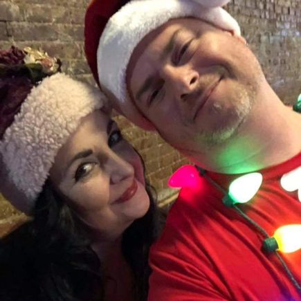Two event attendees wearing Santa hats and holiday accessories posing together for a photo.