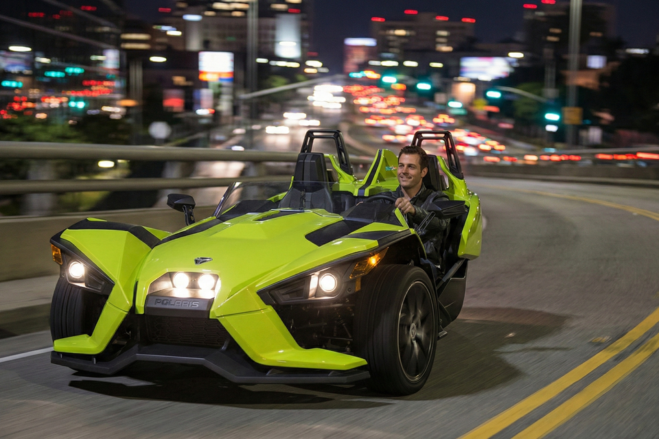 A man in a green slingshot rental driving on the highway at night