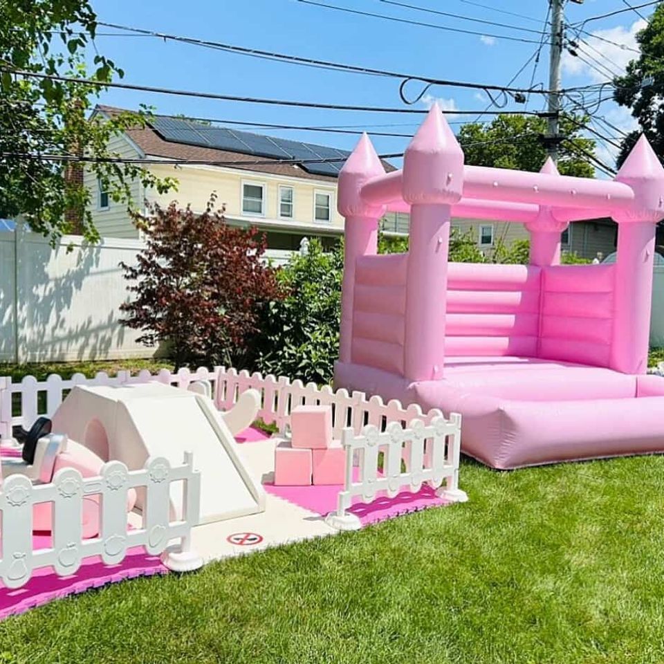 Pink inflatable bounce house with matching soft play area and white picket fence setup for kids’ outdoor party