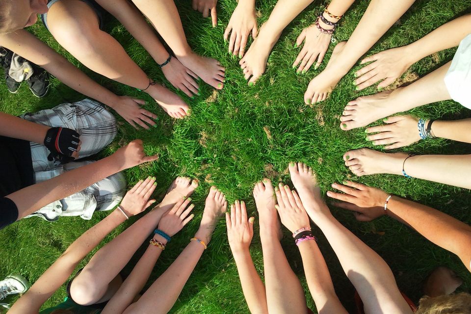 A group of people sitting in a circle on grass, with their hands and feet extended towards the center, creating a sense of unity and teamwork.