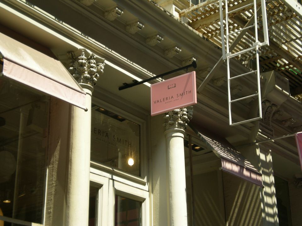 Pink pan-formed blade sign projecting from a cast-iron SoHo facade above a boutique entrance