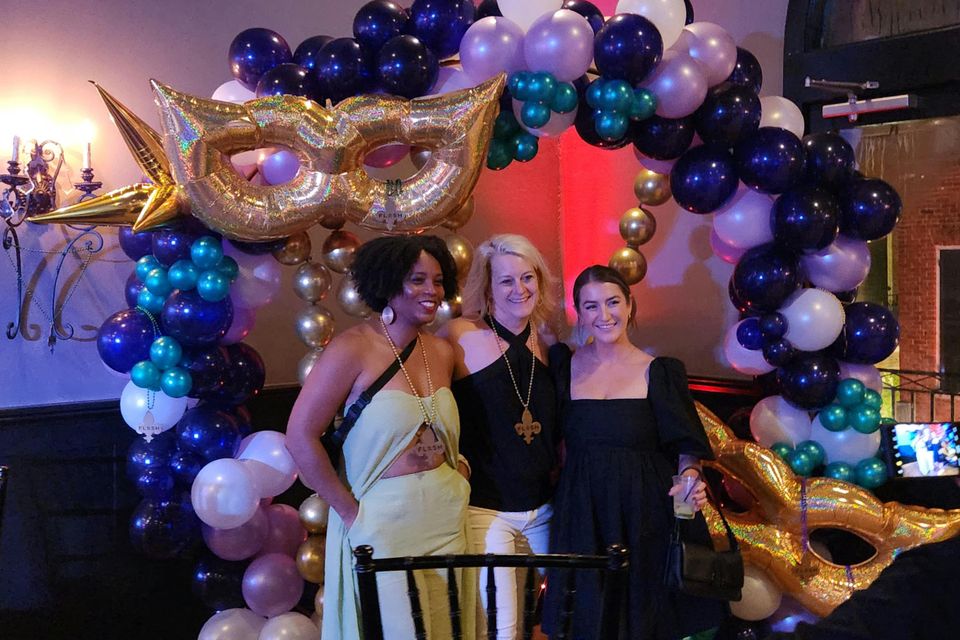 Three ladies in front of a Mardi Gras themed balloon arch.