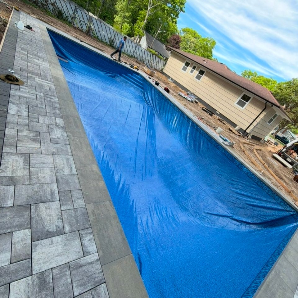New vinyl liner being fitted in a long rectangular inground pool with gray paver decking