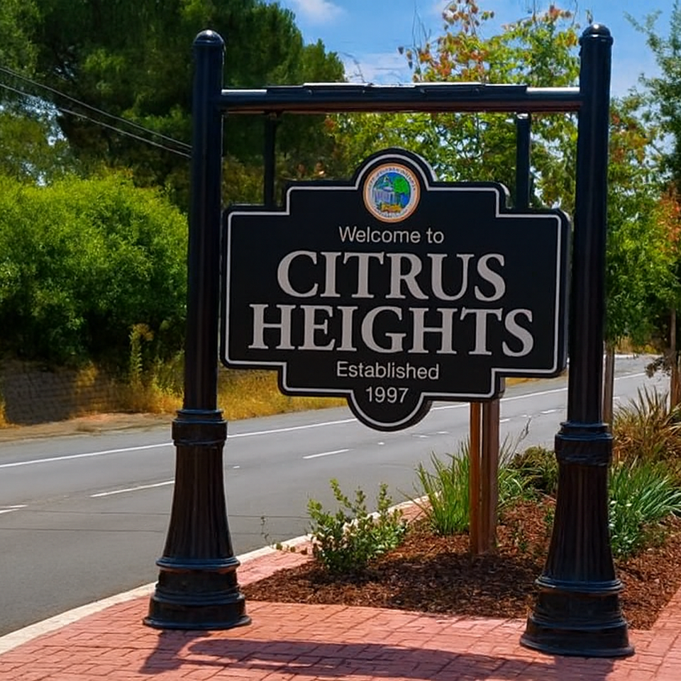 Welcome to Citrus Heights sign on landscaped median with red brick paving, black posts, and surrounding greenery – city entrance landmark in California