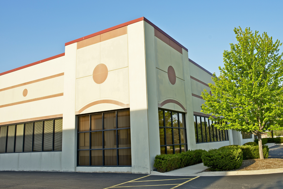 Commercial office building with a modern exterior, large windows, landscaped entrance, and paved parking area.
