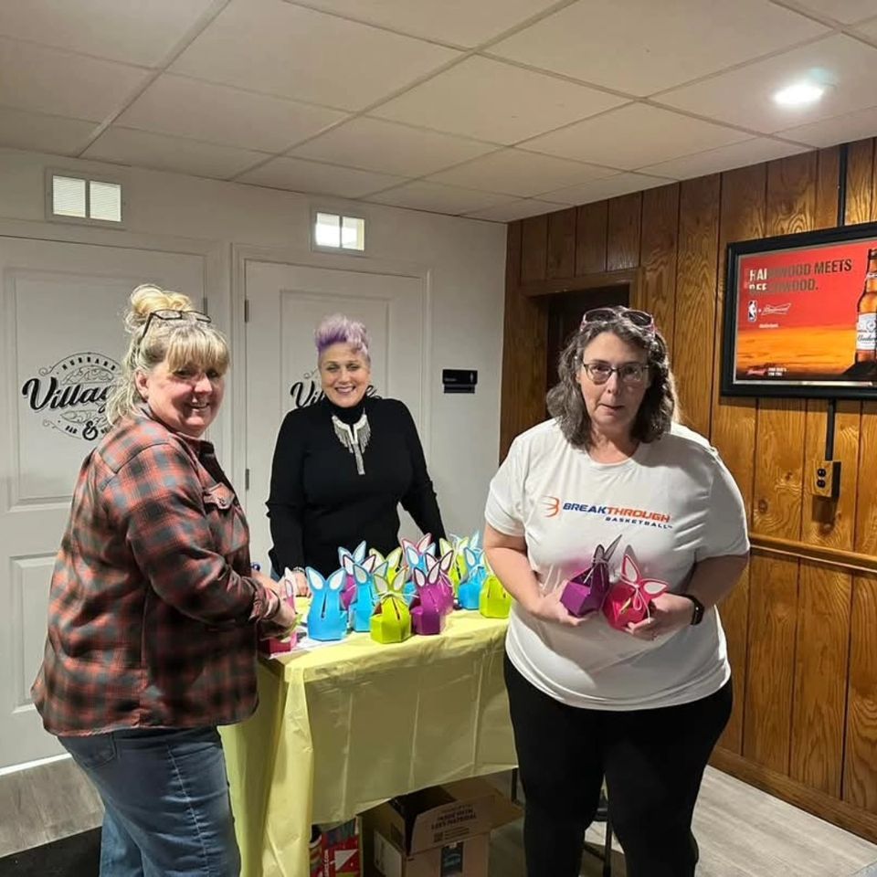 Three volunteers arranging colorful bunny-themed gift boxes on a table at a community event.
