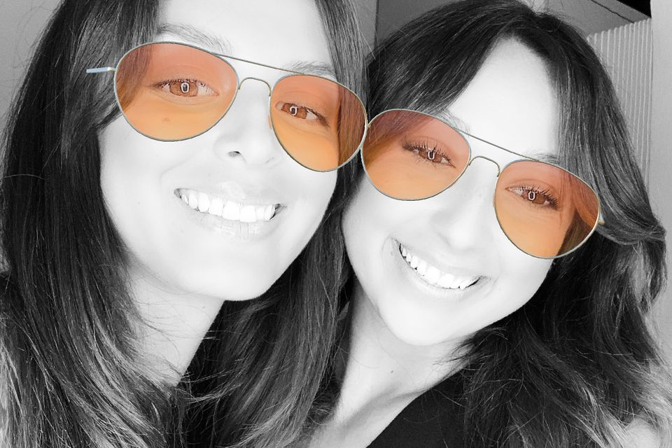 Two women smiling in a glam-style photo booth image with a black-and-white look and tinted sunglasses filter.