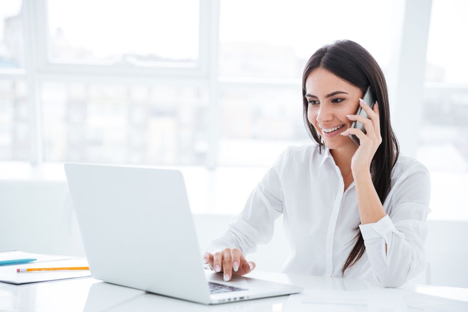 Side view of business woman talking at phone and sitting by the table with laptop in o sbi small