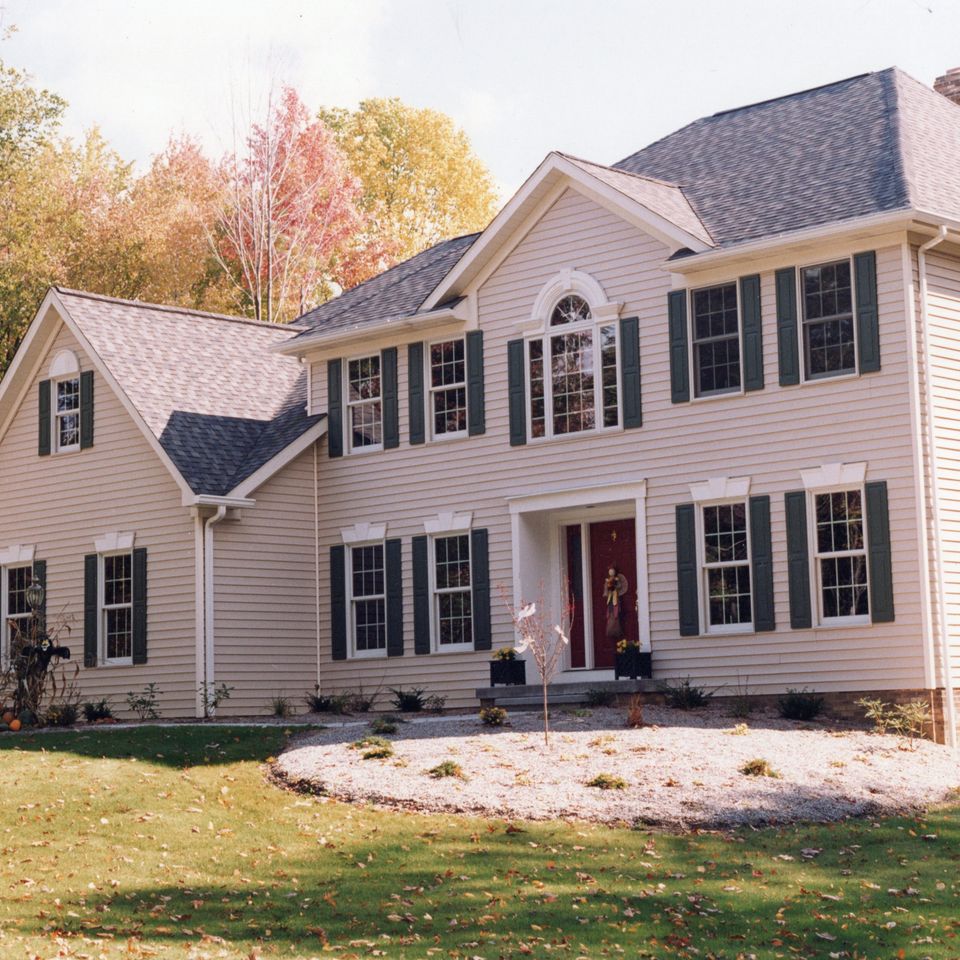 Two-story custom home featuring beige siding, black shutters, a covered front entry, and a landscaped front yard.