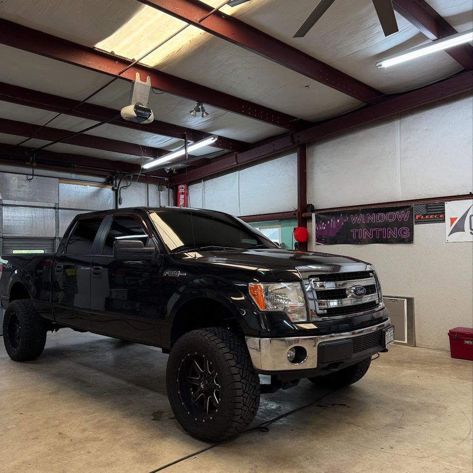 Black lifted Ford F-150 crew cab with tinted windows in the auto tint bay