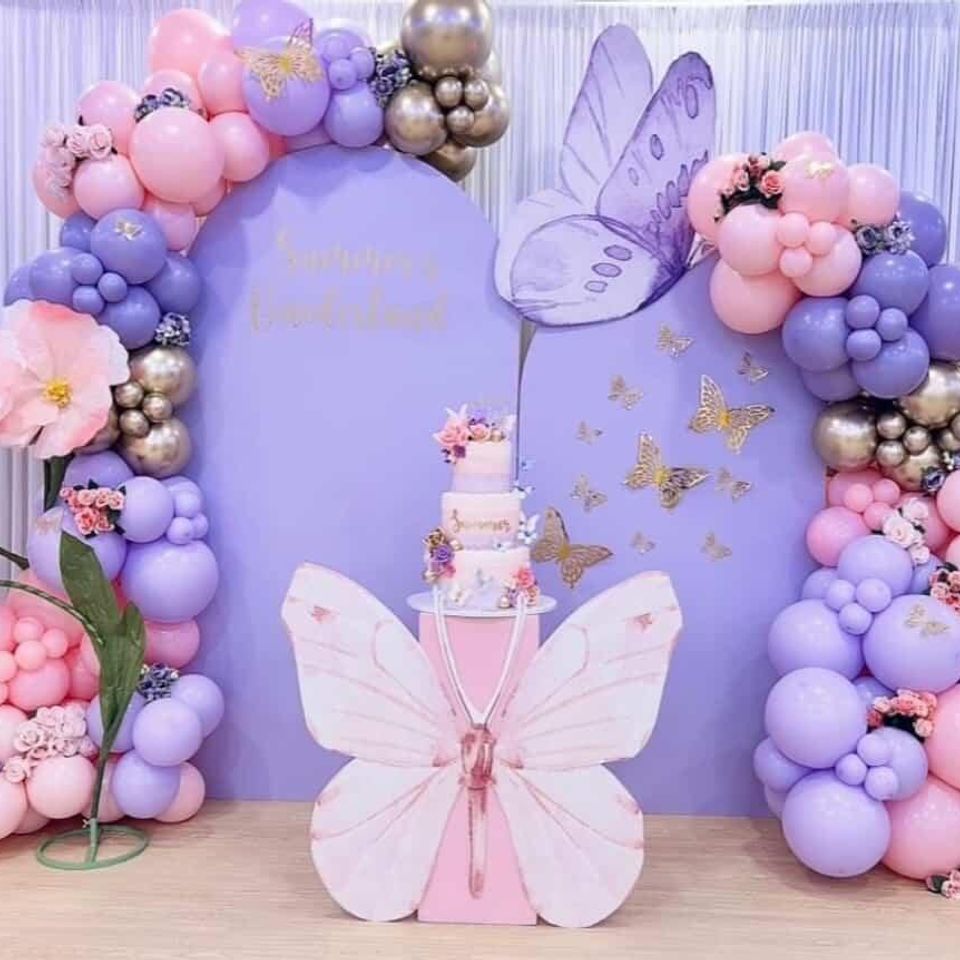 Luxury butterfly-themed event backdrop with purple and pink balloon garlands, gold accents, and a custom cake display by Aldys Events.