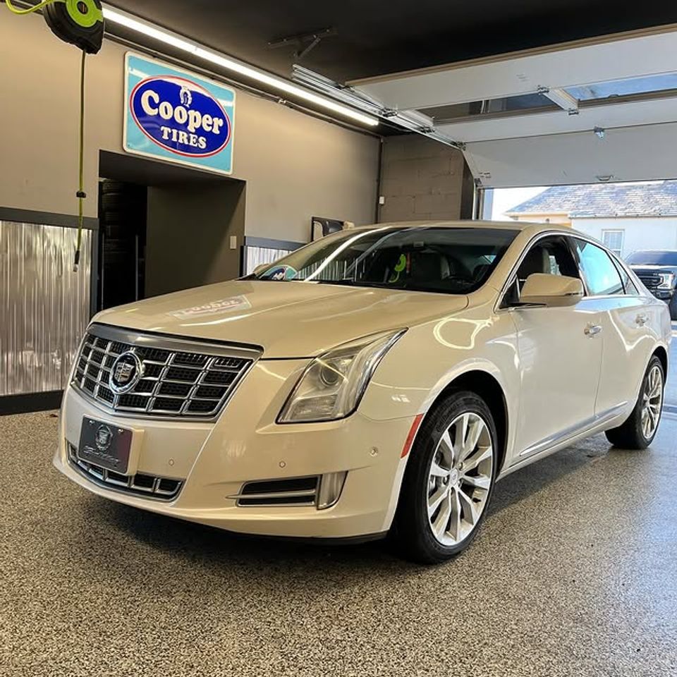 White Cadillac XTS sedan inside tire shop with Cooper Tires sign on wall in Claymont DE