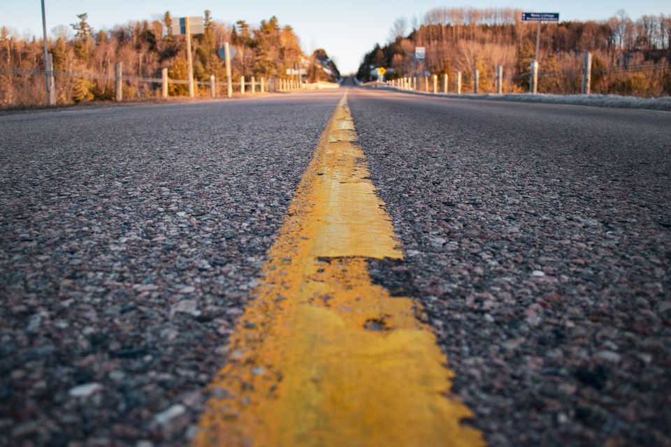 Photo of a road taken at ground level. A yellow line in the middle of the image divides the photo in two halves, as viewers see the road ahead of them.