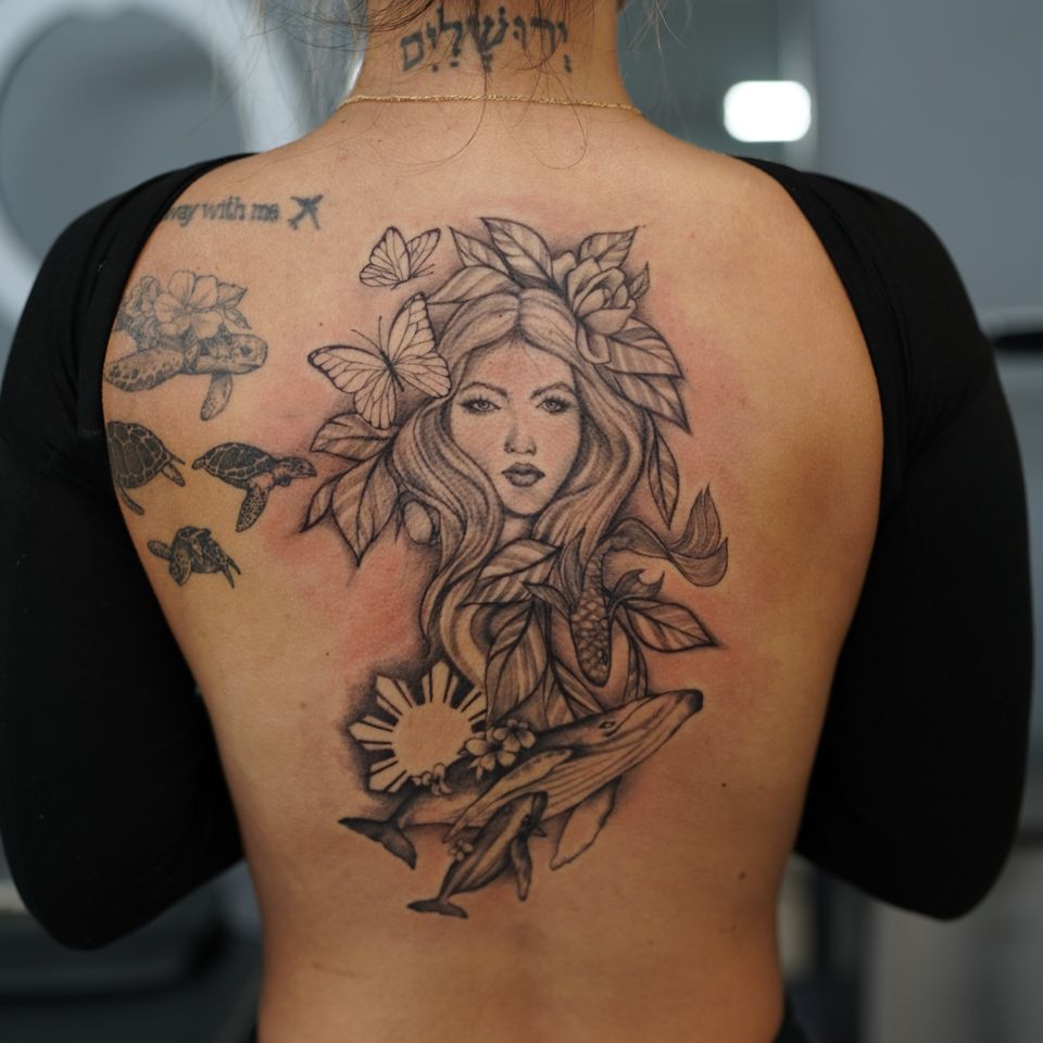 Image of a detailed black and white tattoo of a woman, butterflies, foilage, a whale and it's calf, and sea turtles