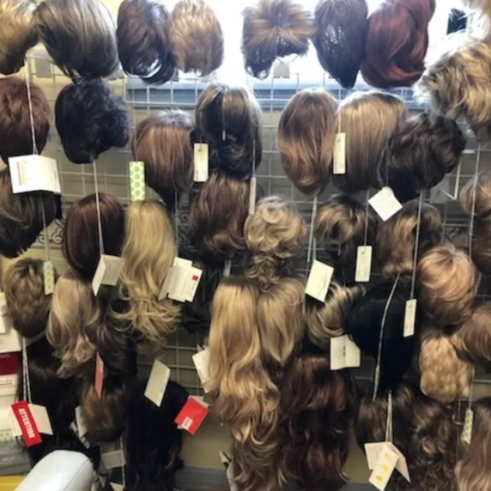 Display of wigs in a variety of colors, lengths, and styles hanging on racks inside Shears Wigs & Hairpieces Salon.