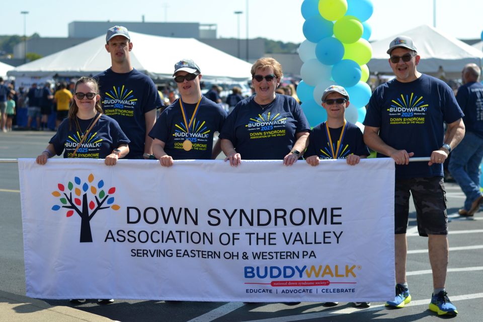 Group of Buddy Walk participants holding a Down Syndrome Association of the Valley banner during a community awareness event.