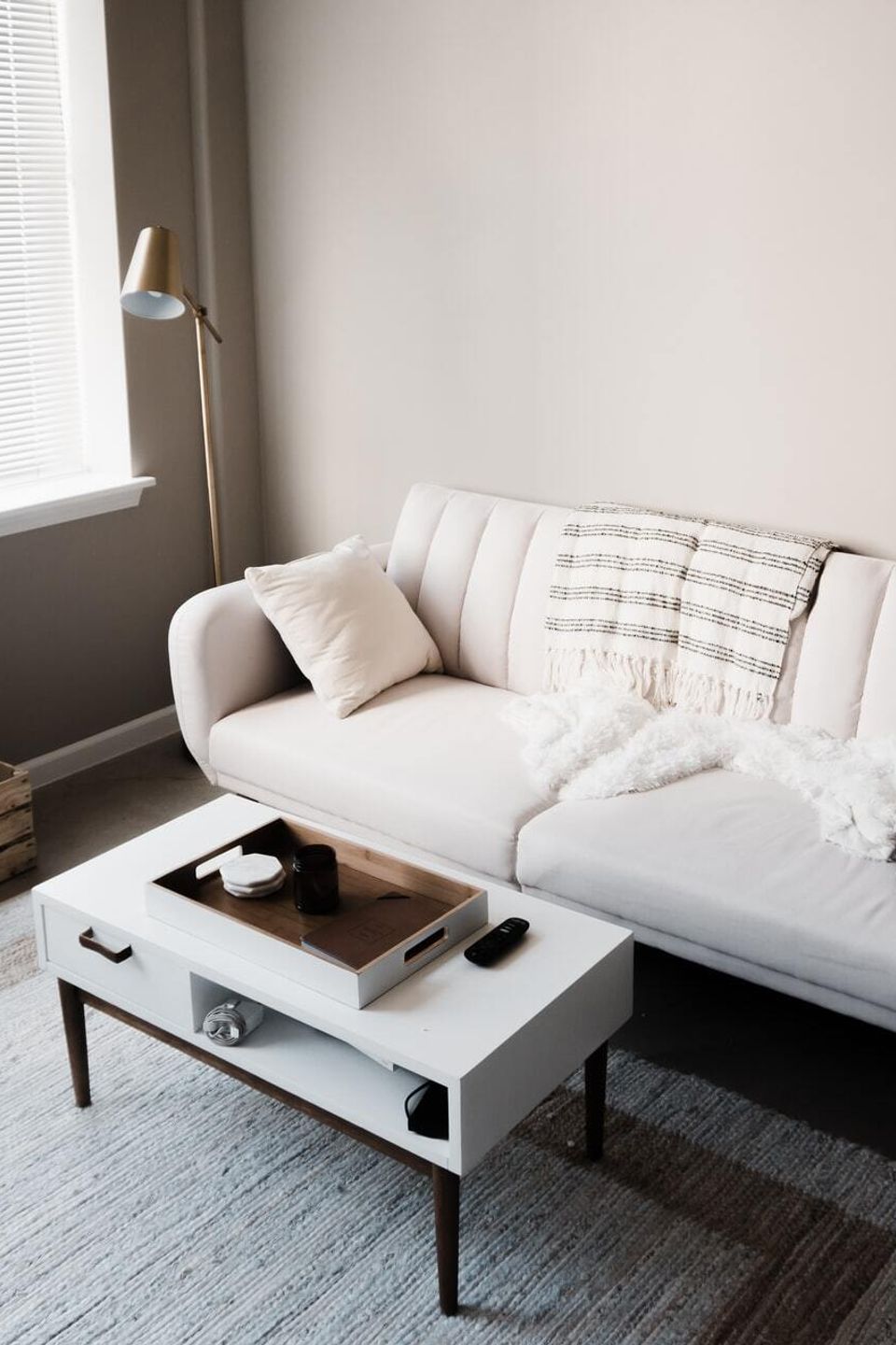 Minimalist living room with light sofa, white coffee table, floor lamp, record player cabinet, and soft natural window light