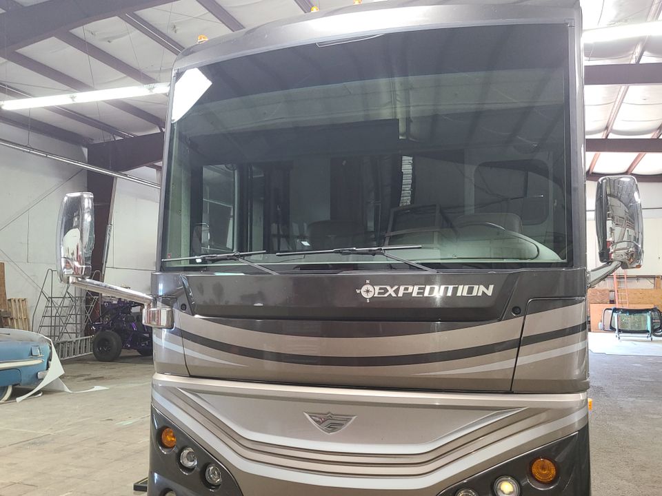 Front view of a motorhome with a newly installed windshield inside a professional RV glass replacement shop.