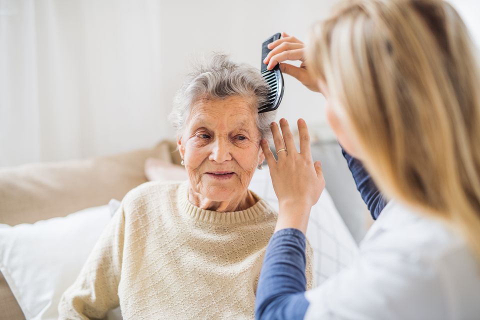 A health visitor combing hair of senior woman at home.