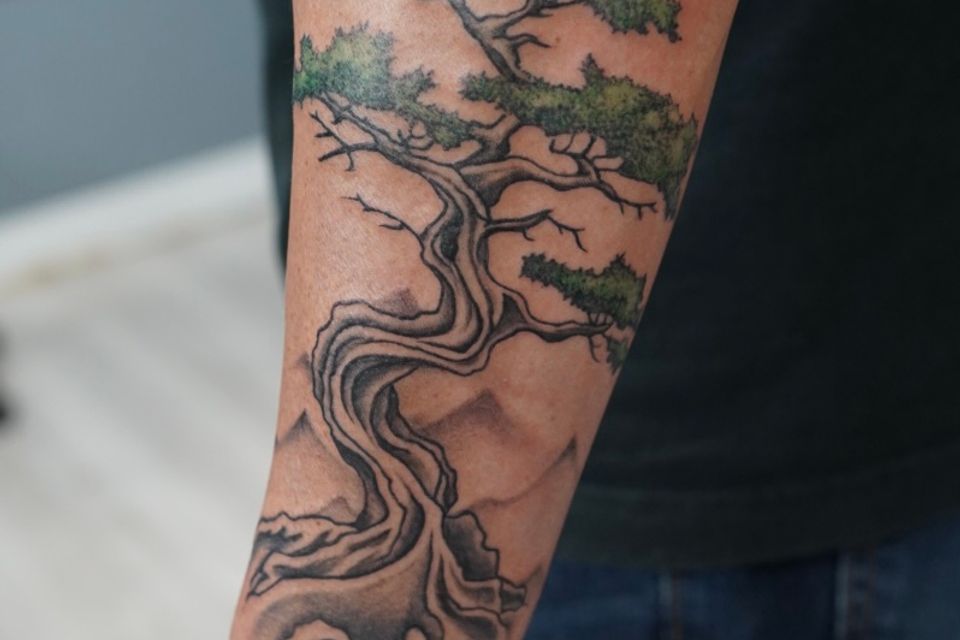 Image of a mans left arm with a Bonsai tree tattoo in black, grey, white and green