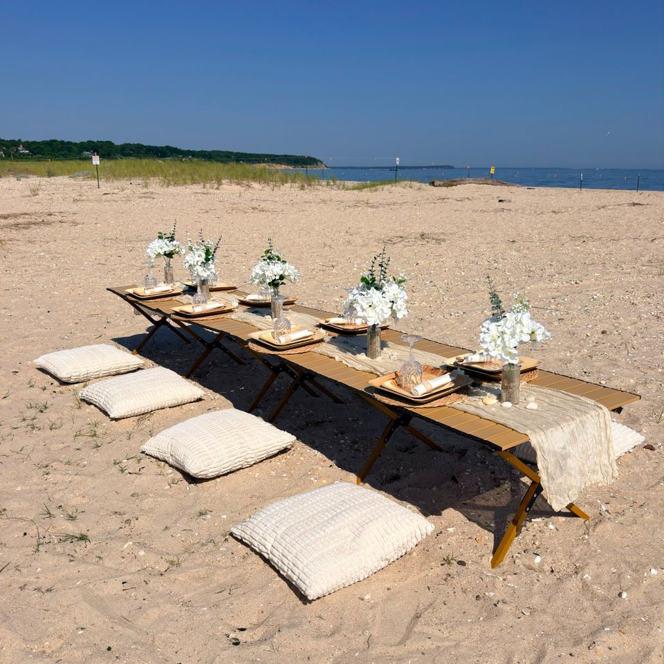 Beach picnic setup with floor cushions and white florals arranged on the sand in the Hamptons