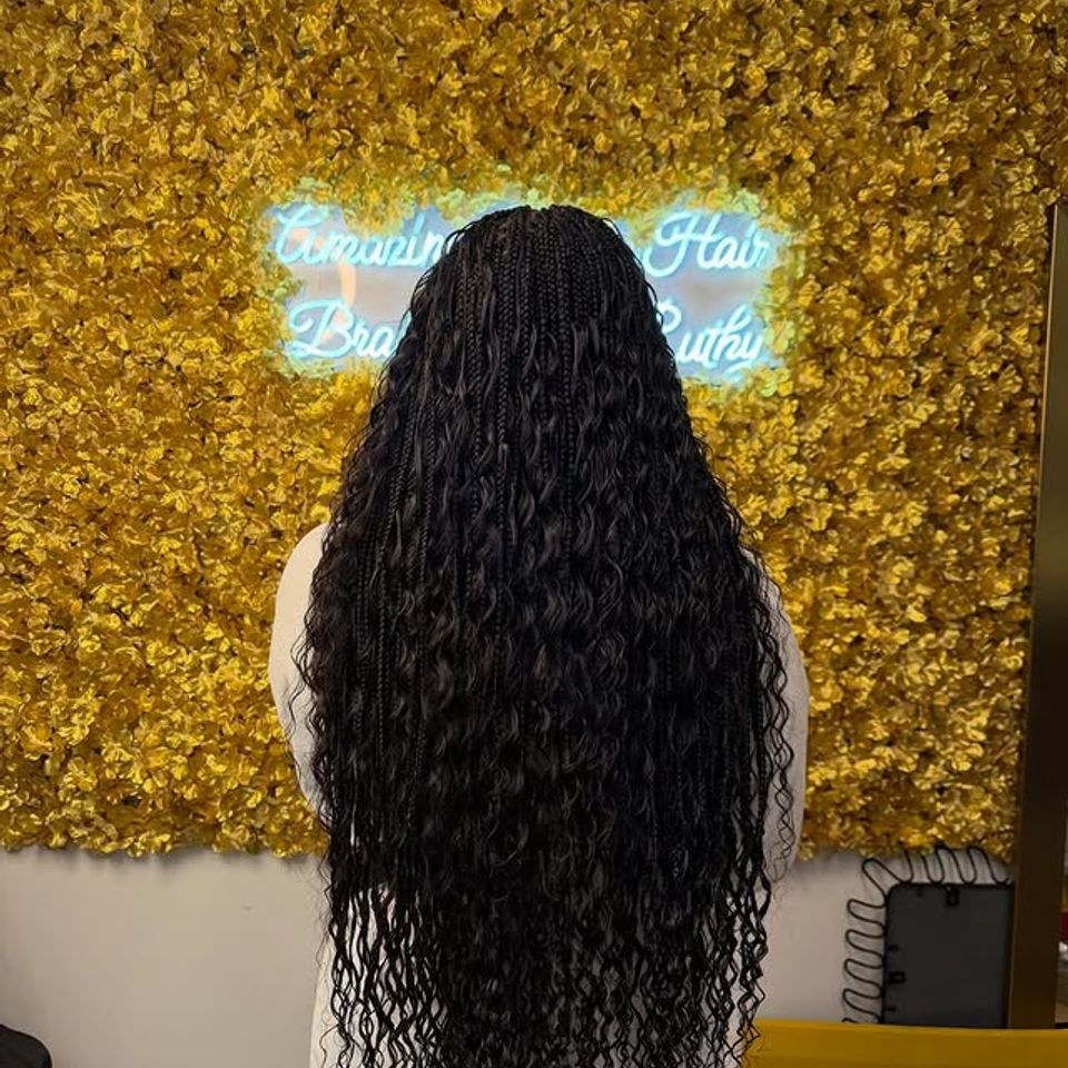 Long boho knotless braids with curly ends in front of the salon neon sign in Los Angeles CA