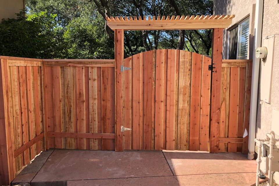 Wooden fence with arched gate and overhead arbor beside residential home