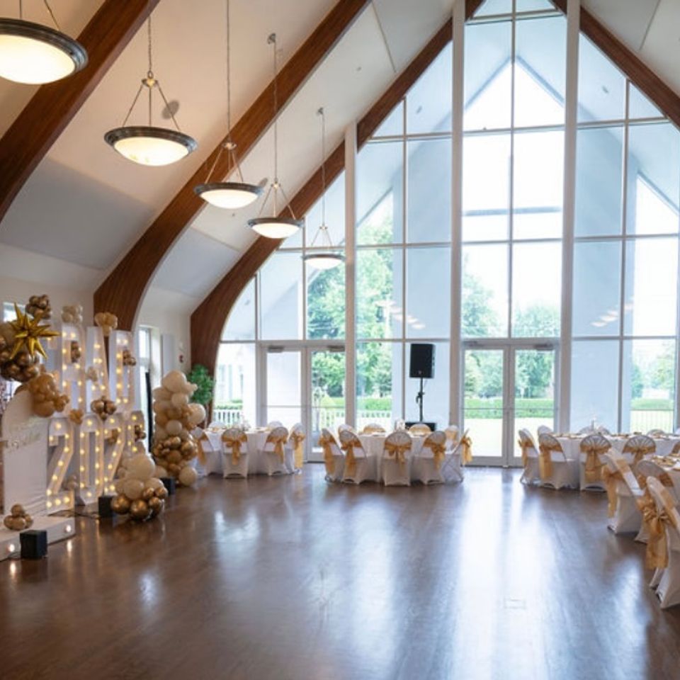 Vaulted event hall set with gold-accented tables and balloon installations for a graduation in the Hamptons NY