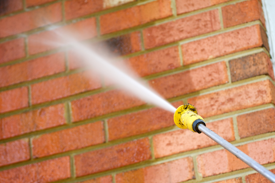 Pressure washing equipment cleaning the exterior brick wall of a residential building to remove dirt, stains, and surface buildup.