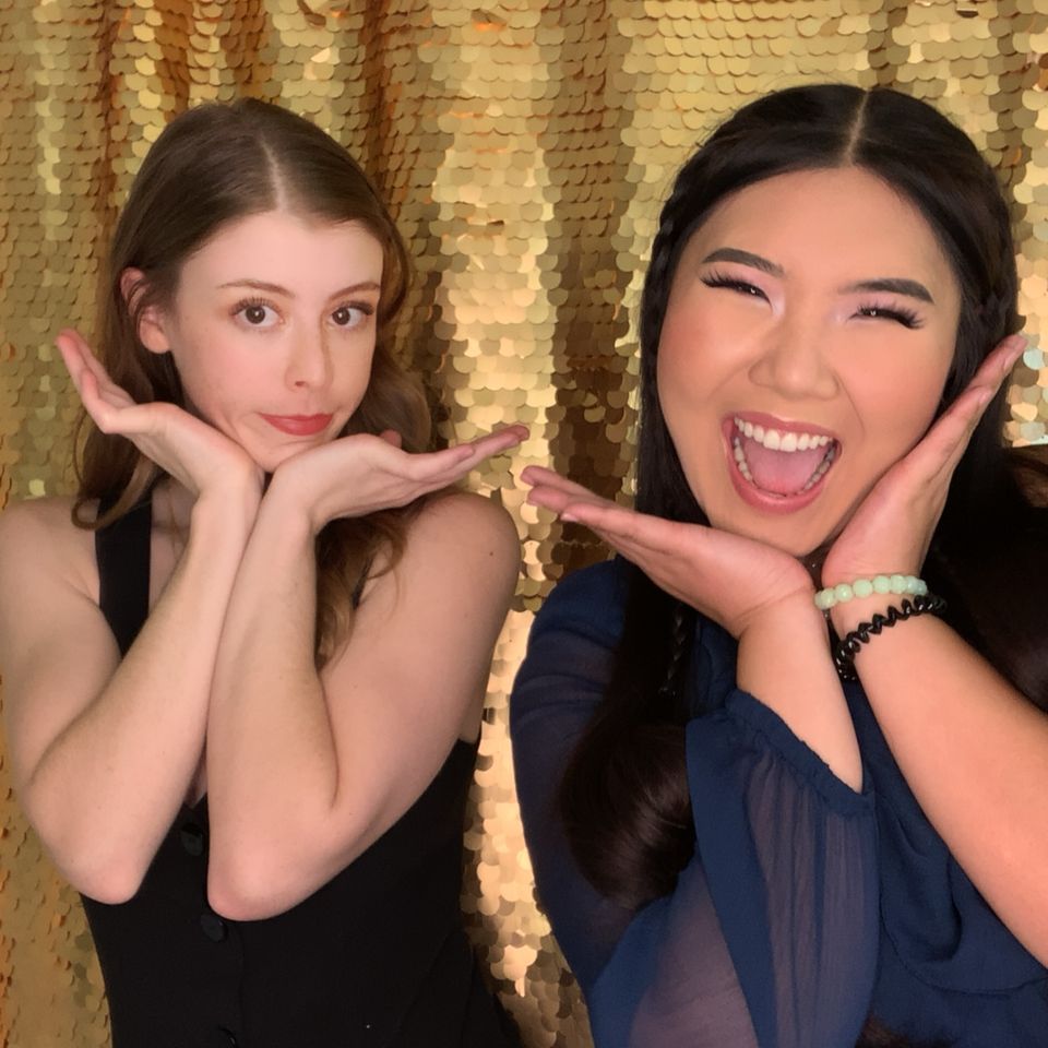 Two women posing playfully in front of a gold sequin backdrop.
