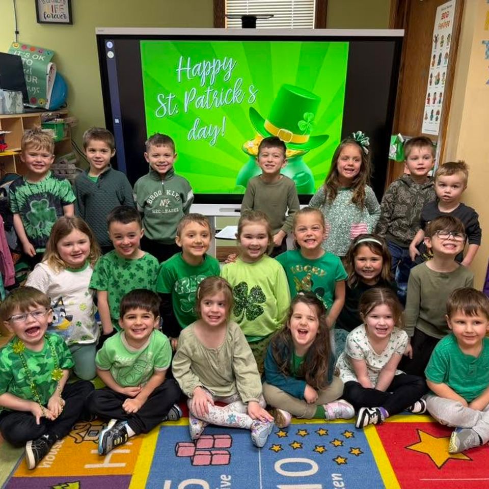Group of kids all wearing green in front of a monitor that says: "Happy St Patrick's Day!"